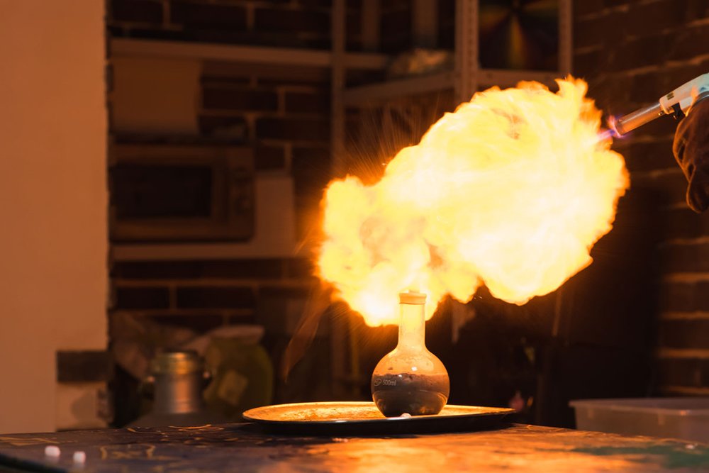 Bild: In einem Labor steht auf einem Tisch ein Gefäß, aus dem Flammen hervorkommen.