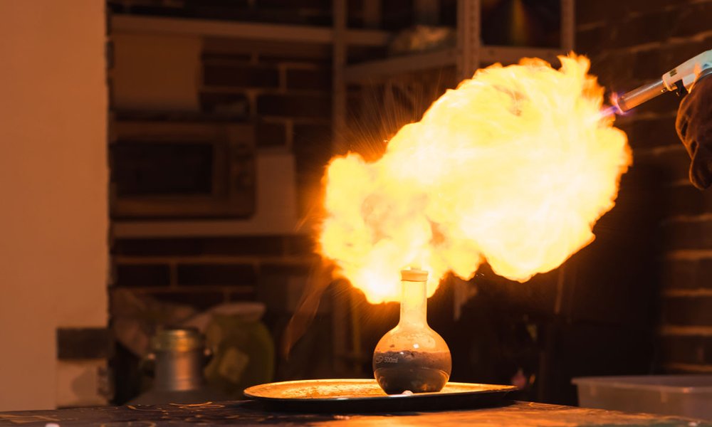 Bild: In einem Labor steht auf einem Tisch ein Gefäß, aus dem Flammen hervorkommen.