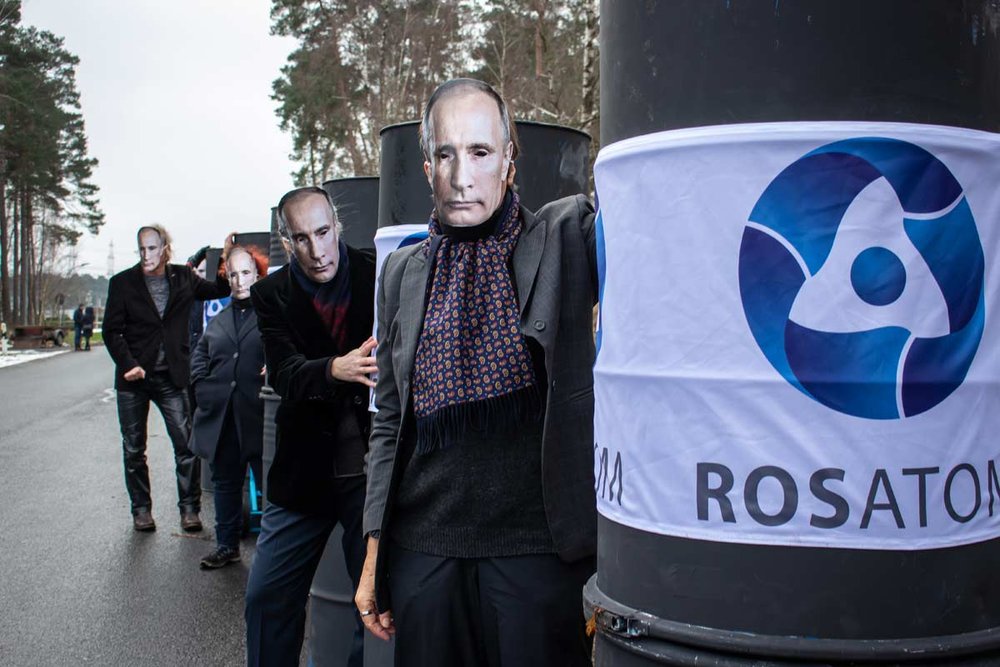 Foto: Menschen mit Putin-Masken mit Fässern, an denen Namen von Atomkonzernen stehen