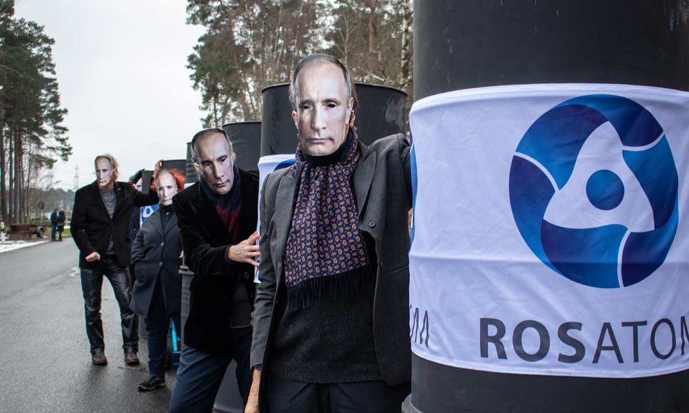 Foto: Menschen mit Putin-Masken mit Fässern, an denen Namen von Atomkonzernen stehen