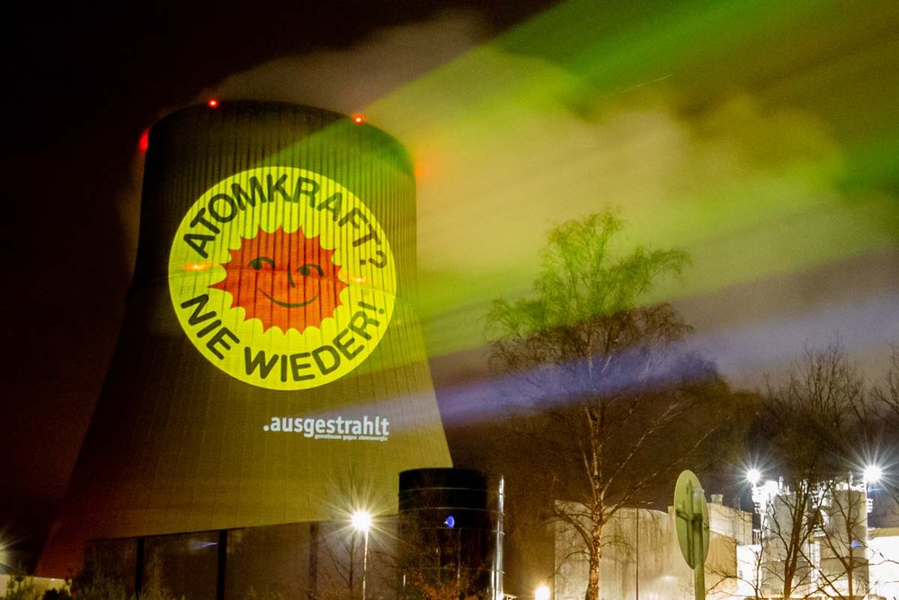 Ein Foto zeigt eine nächtliche Projektion auf einem AKW mit dem Text "Atomkraft? - Nie wieder!"