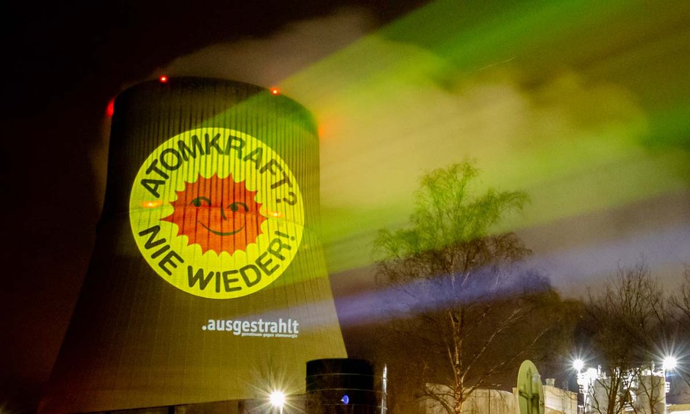 Ein Foto zeigt eine nächtliche Projektion auf einem AKW mit dem Text "Atomkraft? - Nie wieder!"