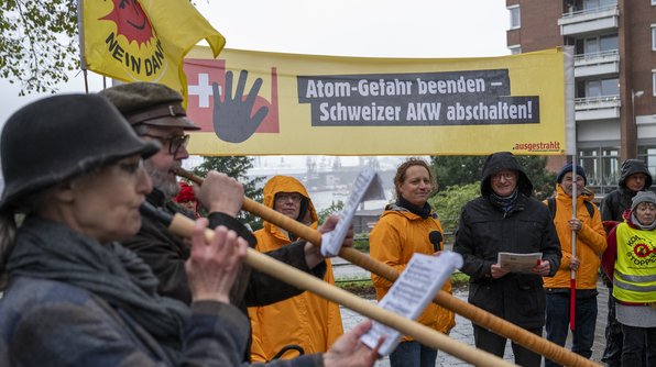 Eine .ausgestrahlt-Demonstration mit Bannern und Transparenten. Auf einem großen gelben Banner steht „Atom-Gefahr beenden – Schweizer AKW abschalten!“. Im Vordergrund spielen zwei Personen Alphörner, während andere Personen Schilder und Flyer hochhalten.