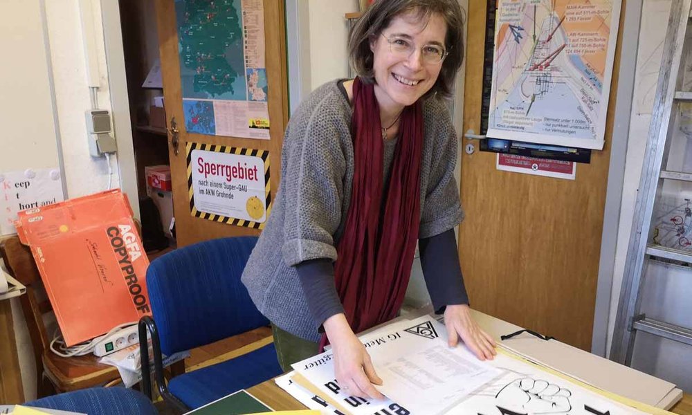 Frau Konstanze Schirmer beugt sich in einem Büro lächelnd über ein Plakat, auf dem steht: Hände weg