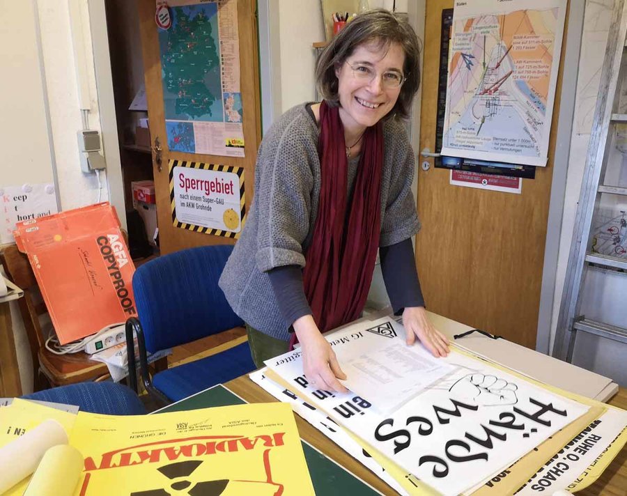 Frau Konstanze Schirmer beugt sich in einem Büro lächelnd über ein Plakat, auf dem steht: Hände weg
