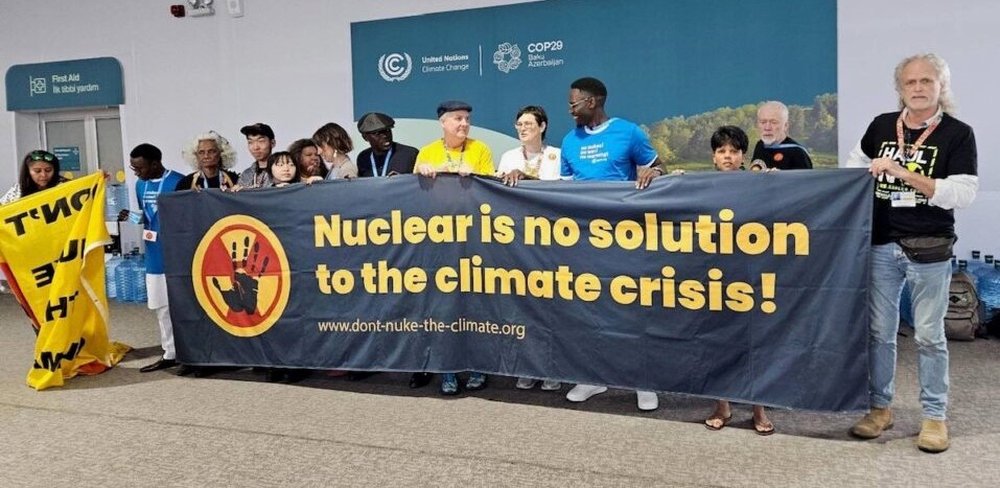 Foto: Menschen vor einem Protest-Banner auf dem COP29 in Baku, 2024