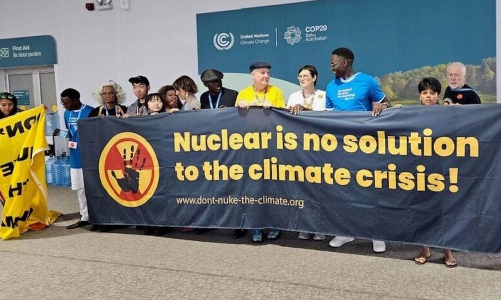 Foto: Menschen vor einem Protest-Banner auf dem COP29 in Baku, 2024