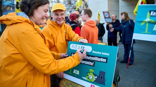Foto: zwei Mitarbeiter*innen von .ausgestrahlt tragen die Anzahl der gesammelten Unterschriften auf einer großen Tafel ein.