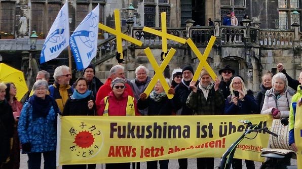 Mehrere Menschen halten während einer Mahnwache gegen Atomkraft Schilder und gelbe Kreuze hoch