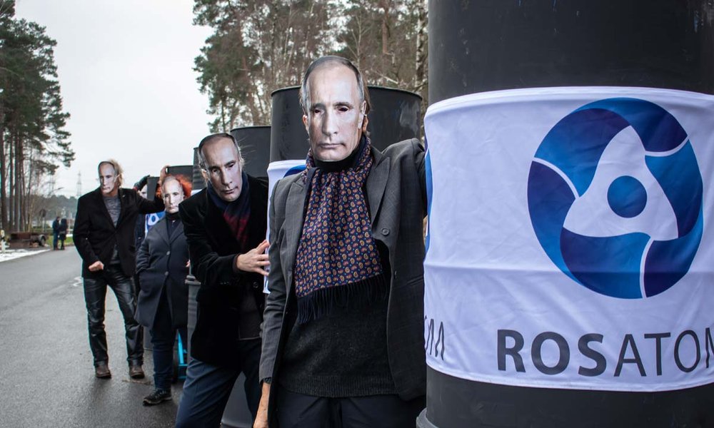 Foto: Menschen mit Putin-Masken und Fässern mit Firmenschriftzug