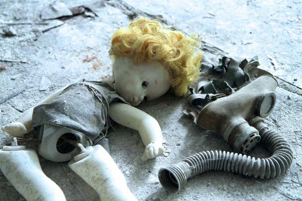Eine kaputte Puppe liegt auf dem Fussboden neben einer Atemschutzmaske