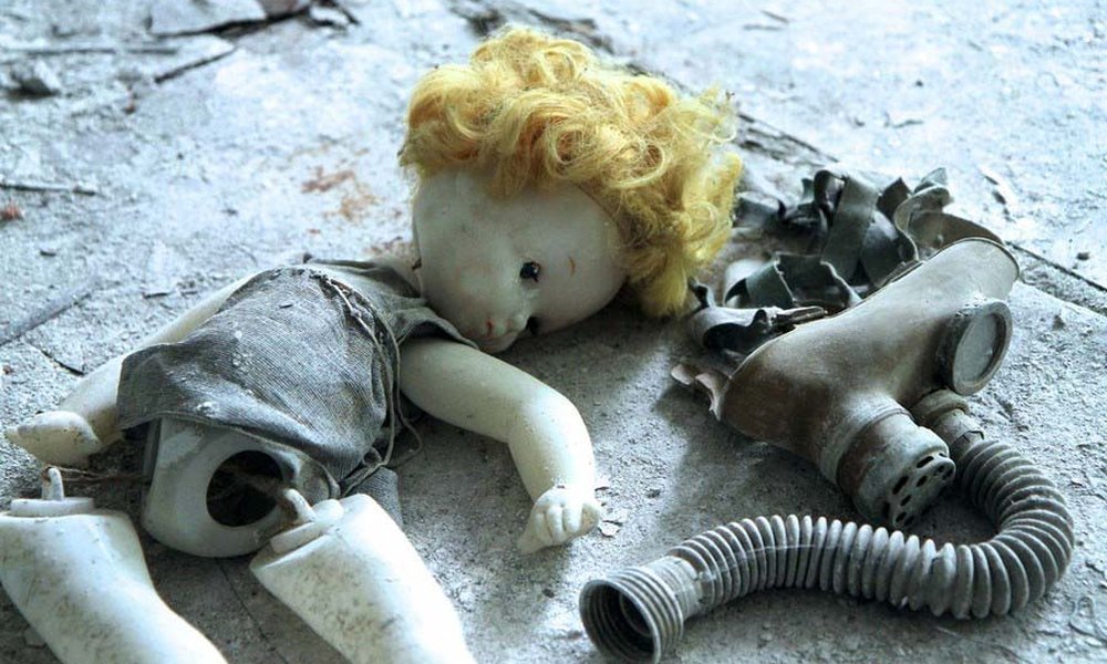 Eine kaputte Puppe liegt auf dem Fussboden neben einer Atemschutzmaske