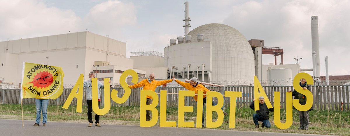 Foto: Atomkraftgegner*innen stehen vor dem AKW Brokdorf und halten große gelbe Buchstaben, die den Satz "aus bleibt aus" ergeben.