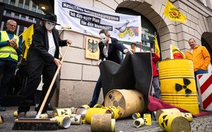 Aktion vor dem Bundesumweltministerium in Berlin. Maskierte Menschen im Anzug fegen mit Atomlogo gekennzeichnete Dosen weg. Anti-Atomkraftfahnen sind ebenfalls zu sehen.